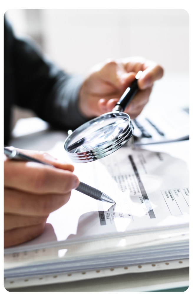 Hands holding a pen and magnifying glass examining papers.