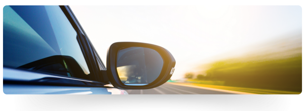 Close-up view of a car's side mirror, capturing the sense of speed and motion with a blurred background, suggesting the vehicle is moving swiftly down a road