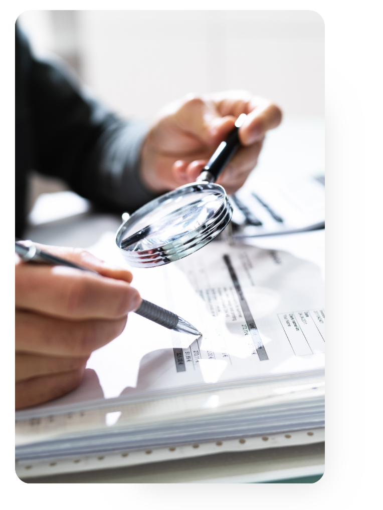 Hands holding a pen and magnifying glass examining papers.